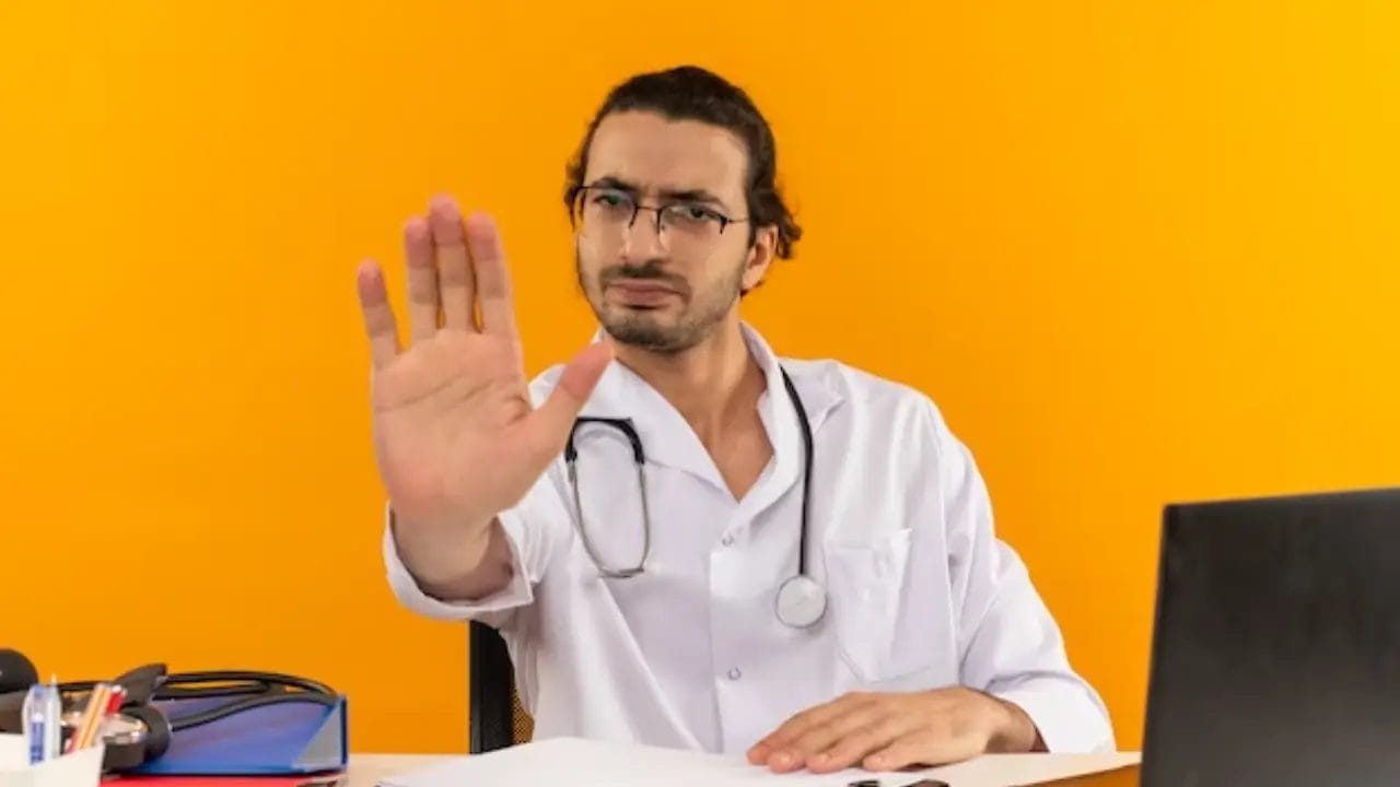 طبيب يجلس على مكتبه و يشير بيده للشاشة بعلامة توقف